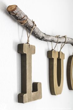 three wooden letters hang from a branch on the wall next to two small hooks that spell out love