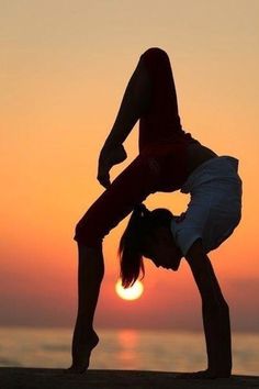 a woman doing a handstand on the beach at sunset