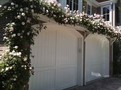 an arch covered in flowers next to two garage doors with windows on each side and one door open