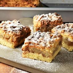 four pieces of dessert sitting on top of a metal baking pan with powdered sugar