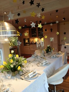 a dining room table is set with white and yellow flowers, silverware and candles