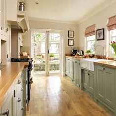 a large kitchen with green cabinets and wood flooring on the counter top, along with a sink