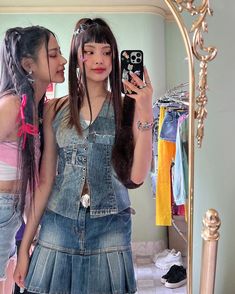 two girls standing in front of a mirror looking at their cell phones