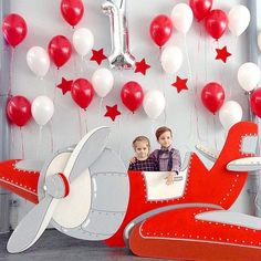 two young boys are sitting in an airplane with red and white balloons