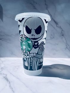 a starbucks cup with a skeleton on it sitting on a marble countertop next to a black and white wall