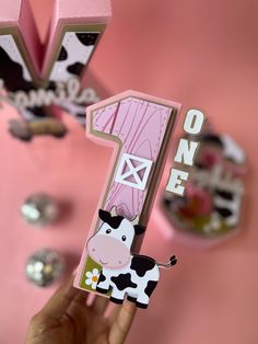 a person holding up a pink one - letter shaped card with a cow on it