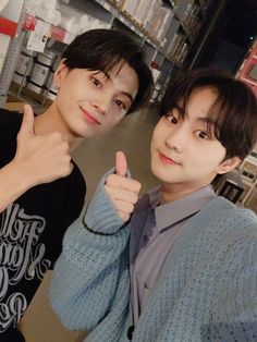 two young men standing next to each other giving the thumbs up sign in a store