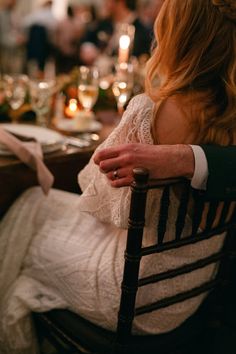 a woman sitting in a chair at a dinner table with candles and wine glasses on it