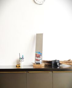 a clock on the wall above a desk with a camera and other items sitting on it