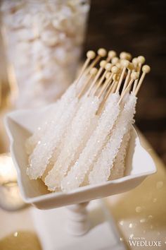 several skewered food items in a white dish on a table with candles behind it