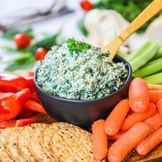 a plate with carrots, crackers and spinach dip on it next to other vegetables