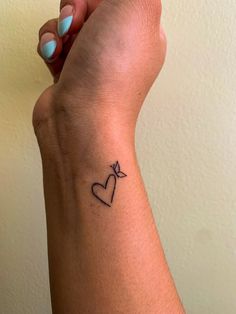 a woman's arm with a small heart tattoo on her left wrist and an arrow in the middle