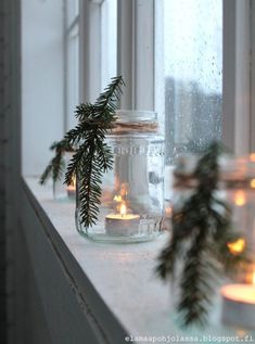 candles are sitting on a window sill in front of the windowsill and evergreen branches