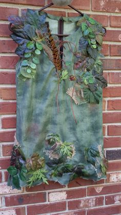 a piece of clothing hanging on the side of a brick wall with leaves and plants all over it