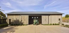 a tractor is parked in front of a barn with two doors and a metal roof