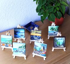 small easels with paintings on them sitting on a table next to a potted plant