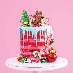 a christmas cake with icing, candy and decorations on a white pedestal against a pink background