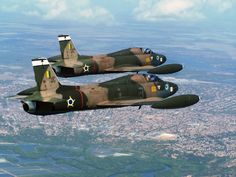 two fighter jets flying in the sky over a cityscape and riverbeds