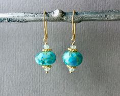 "⇩CLICK BELOW FOR DETAILS⇩ ✦These hand blown turquoise blue green lampwork bead earrings are magnificent. Each handmade lampwork abstract glass borosilicate bead, measures 10mm x 14mm and is filled with gorgeous blues and turquoise to create a stunning look. The beads are adorned with beautiful gold daisy spacers and wire wrapped to sturdy 18k gold vermeil round hook ear wires. Earring length is about 1.25 inches. ✦Your jewelry will be packaged in a beautiful and reusable organza bag. All items Turquoise Glass Earrings For Gift, Turquoise Jewelry With French Hook For Gift, Turquoise Czech Glass Earrings As Gift, Hypoallergenic Turquoise Glass Earrings, Turquoise Glass Round Bead Earrings, Handmade Turquoise Murano Glass Jewelry, Unique Turquoise Czech Glass Earrings, Unique Turquoise Earrings With Czech Glass, Turquoise Wire Wrapped Czech Glass Earrings