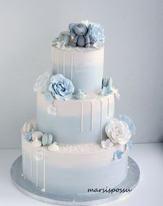 a three tiered white wedding cake with blue flowers on the top and two teddy bears atop it