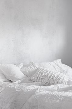 an unmade bed with white sheets and pillows