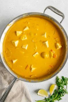 a pot filled with yellow soup next to some lemon wedges and cilantro