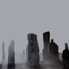 some very tall rocks in the water with fog coming off them and one person standing on it