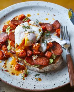 a white plate topped with an egg, bacon and tomato sandwich next to a fork