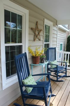 two blue rocking chairs sitting on a wooden porch next to a potted plant and window