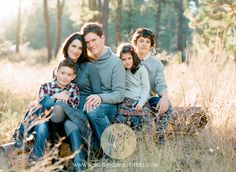 a family sitting on a log in the middle of a field with tall grass and trees