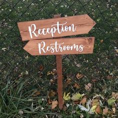 a wooden sign sitting in the grass next to a chain link fence that says reception restrooms