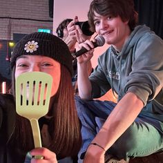 two people are sitting on the floor and one is holding a spatula while the other holds a microphone