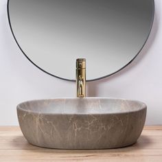 a bathroom sink with a round mirror on the wall above it and a gold faucet