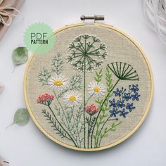 an embroidery pattern with flowers and leaves on the hoop, next to some thread spools