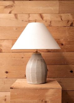 a white lamp sitting on top of a wooden table next to a wall covered in wood planks