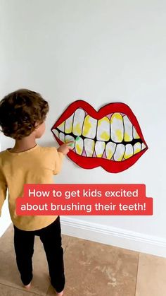 a little boy standing in front of a white wall with a red and yellow teeth on it