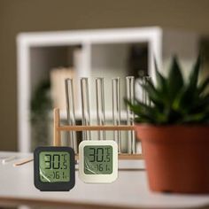 two clocks sitting on top of a table next to a potted plant