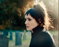 a woman with black hair standing in front of a cemetery and looking off into the distance