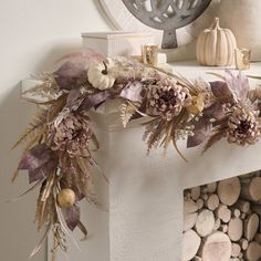 a white fireplace mantle with dried flowers and leaves on it, along with other decorations