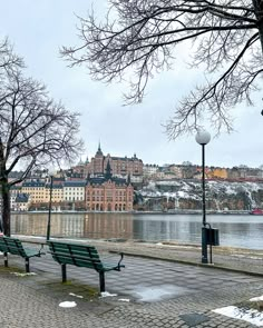 two park benches sitting next to each other on a sidewalk near the water and buildings