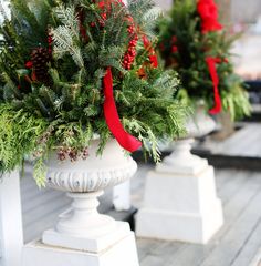 three white urns with evergreen and red ribbon tied around them on a wooden deck