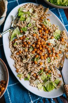 a white plate topped with pasta and lettuce covered in chickpeas next to bowls of salad