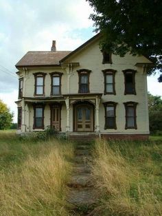 an old white house with tall grass in front of it and a path leading to the door