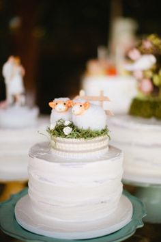 two small sheep on top of a wedding cake with moss and flowers in the middle