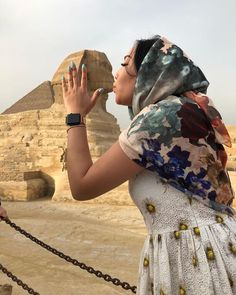 a woman standing in front of the pyramids with her hands up to her face