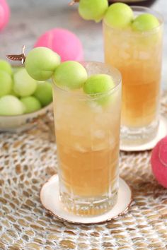 two glasses filled with drinks sitting on top of a table next to green and pink balls