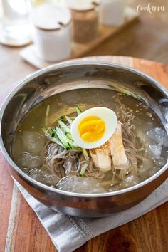 an egg is sitting on top of noodles in a bowl with water and ice cubes