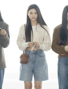 three young women standing in front of a window looking at their cell phones and purses