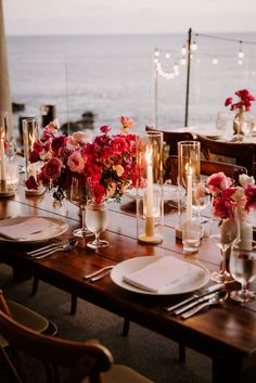 a table set for dinner with candles and flowers in vases on the table next to the ocean