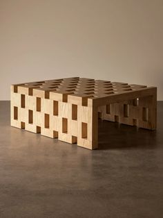 a wooden bench made out of squares on top of a cement floor in front of a wall